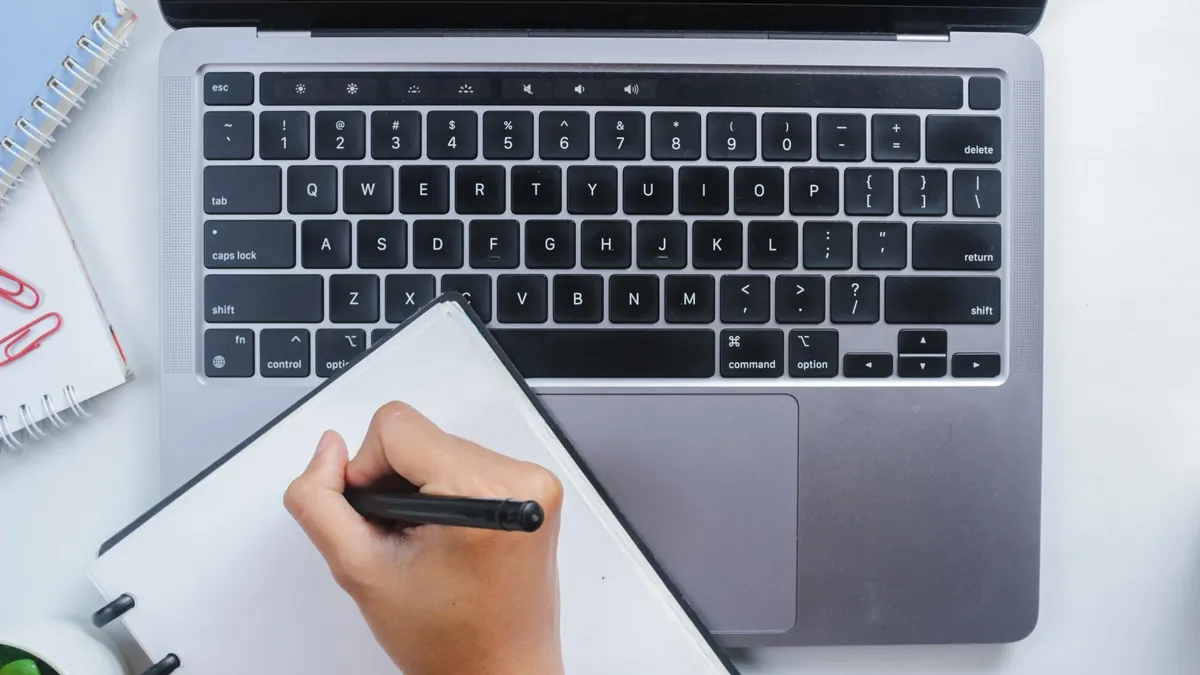 Writer editing press release copy in a notebook beside a laptop